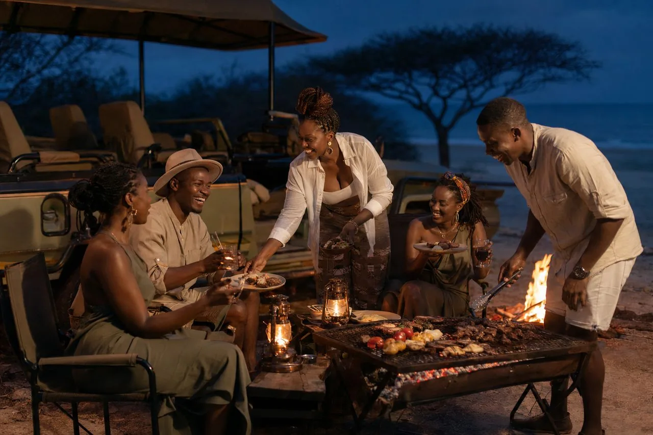 Tanzanian friends sharing a bonfire dinner on the beach at dusk at Saadani, lanterns glowing and the ocean beyond